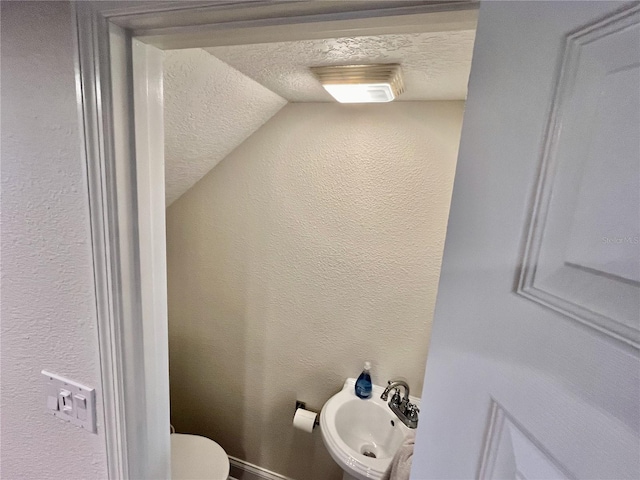 bathroom with sink, toilet, vaulted ceiling, and a textured ceiling