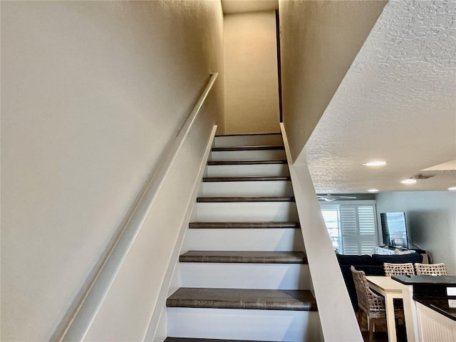 stairs featuring ceiling fan and a textured ceiling