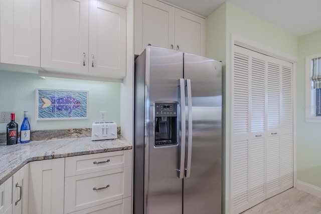 kitchen with stainless steel refrigerator with ice dispenser, light stone countertops, and white cabinets