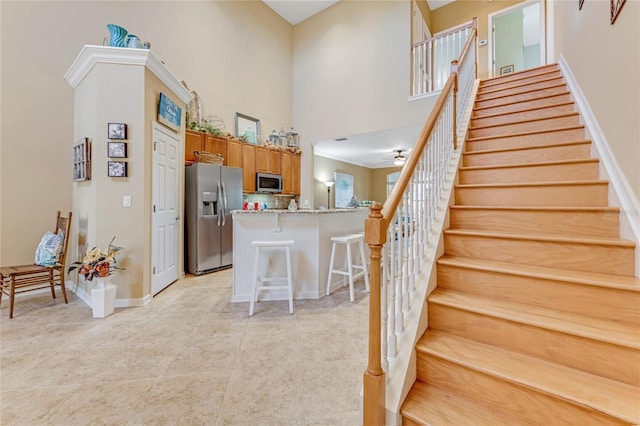 kitchen with a towering ceiling, a breakfast bar, ceiling fan, kitchen peninsula, and stainless steel appliances