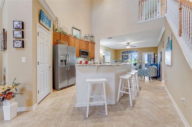 kitchen featuring ceiling fan, appliances with stainless steel finishes, light stone counters, ornamental molding, and a kitchen bar