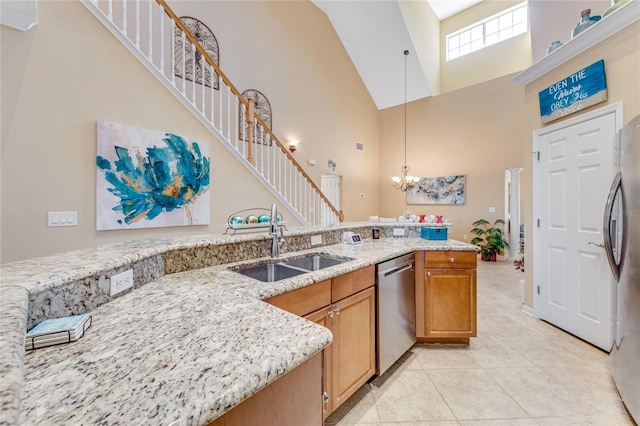 kitchen with appliances with stainless steel finishes, a towering ceiling, pendant lighting, sink, and light stone counters