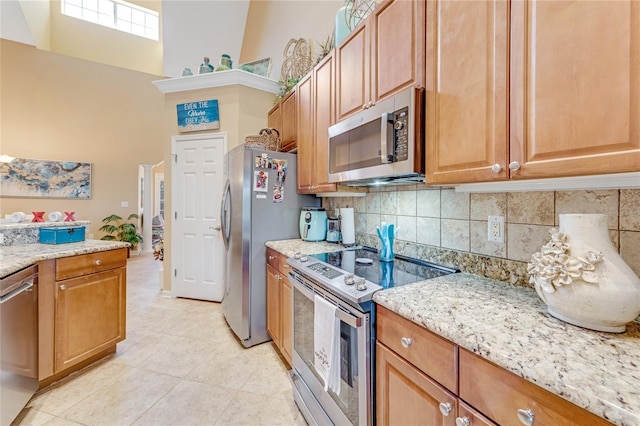 kitchen with stainless steel appliances, light tile patterned floors, light stone counters, and decorative backsplash