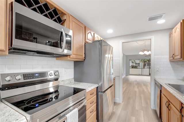 kitchen featuring light hardwood / wood-style flooring, stainless steel appliances, light stone countertops, decorative light fixtures, and light brown cabinets