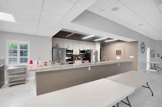 kitchen with a breakfast bar, appliances with stainless steel finishes, white cabinetry, light stone counters, and a drop ceiling