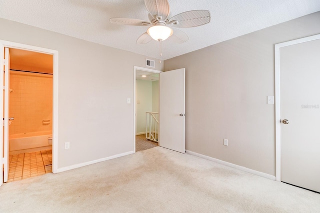 unfurnished bedroom featuring a textured ceiling, connected bathroom, light colored carpet, and ceiling fan