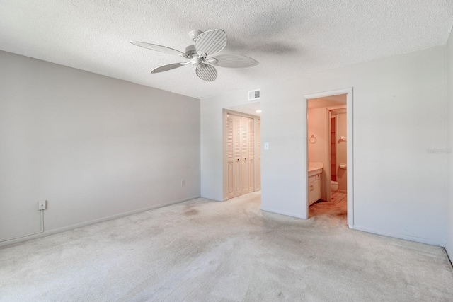 unfurnished bedroom with a textured ceiling, ensuite bath, a closet, and ceiling fan