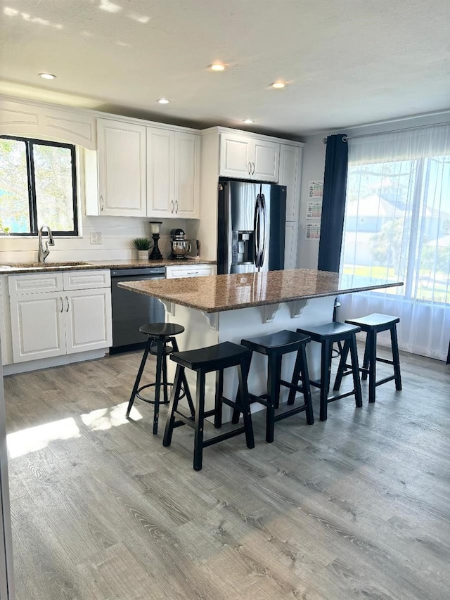 kitchen with stainless steel refrigerator with ice dispenser, a breakfast bar, white cabinetry, black dishwasher, and a kitchen island