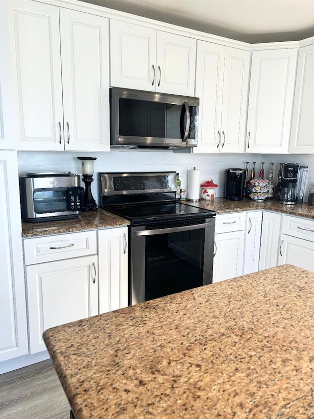 kitchen with stainless steel appliances, white cabinetry, light stone counters, and light wood-type flooring