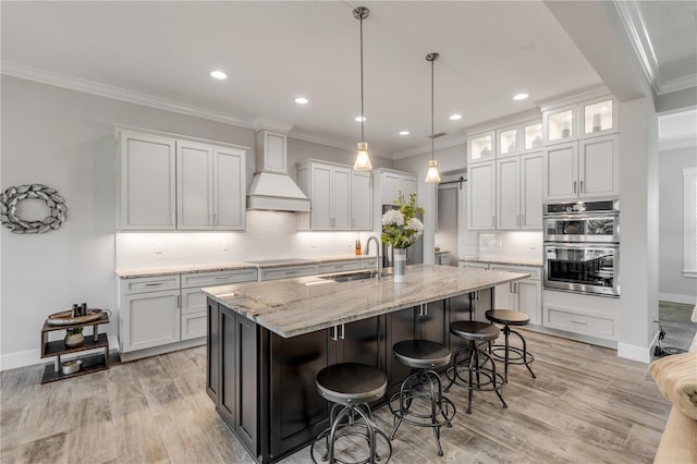 kitchen with a kitchen island with sink, sink, stainless steel double oven, and white cabinets