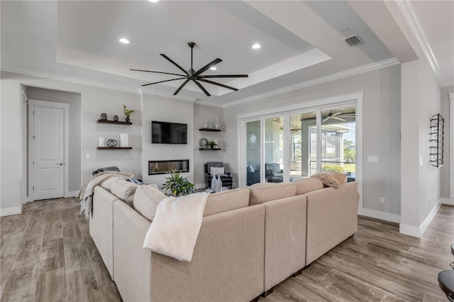 living room featuring ornamental molding, light hardwood / wood-style flooring, ceiling fan, and a tray ceiling