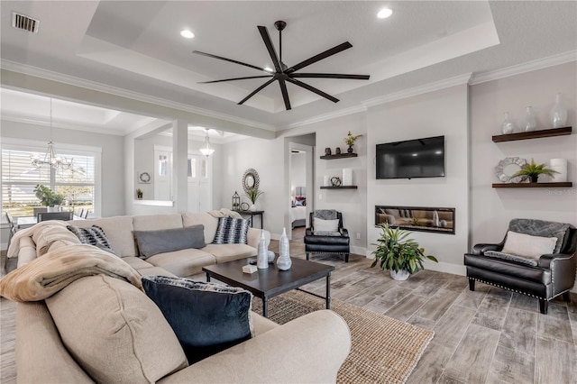 living room featuring ornamental molding, a raised ceiling, and ceiling fan with notable chandelier