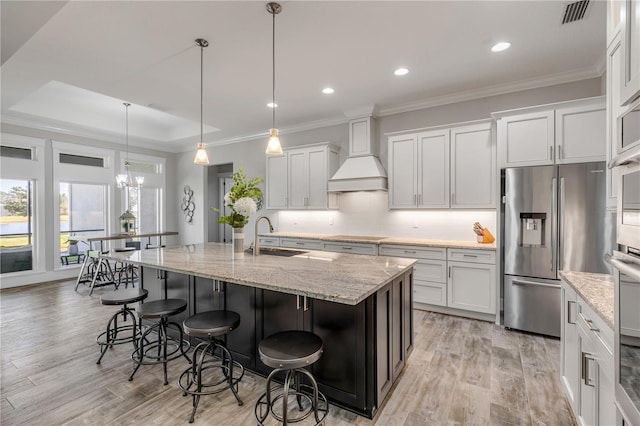 kitchen featuring a kitchen island with sink, custom range hood, white cabinets, and stainless steel refrigerator with ice dispenser