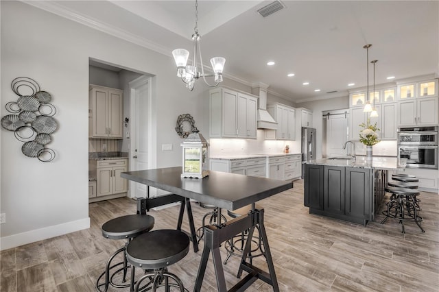 kitchen with decorative light fixtures, tasteful backsplash, sink, white cabinets, and a kitchen island with sink