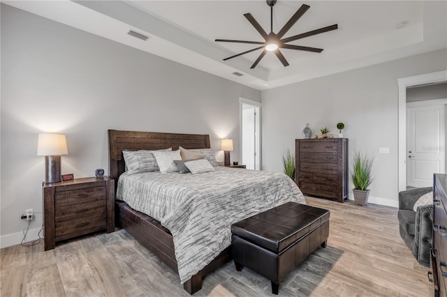 bedroom with ceiling fan, a tray ceiling, and light wood-type flooring