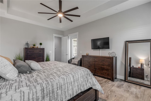 bedroom with light wood-type flooring, ceiling fan, and a tray ceiling