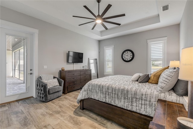 bedroom with ceiling fan, a tray ceiling, access to exterior, and light hardwood / wood-style flooring