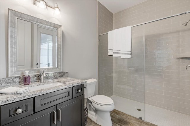 bathroom with tiled shower, vanity, toilet, and wood-type flooring