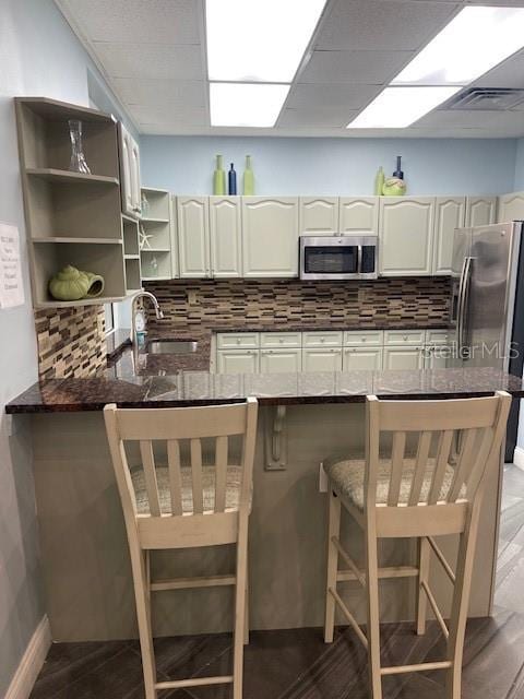 kitchen with appliances with stainless steel finishes, a breakfast bar, tasteful backsplash, white cabinets, and kitchen peninsula