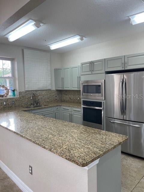 kitchen featuring gray cabinets, sink, decorative backsplash, kitchen peninsula, and stainless steel appliances