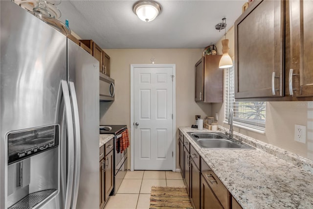 kitchen with appliances with stainless steel finishes, decorative light fixtures, sink, light tile patterned floors, and light stone counters