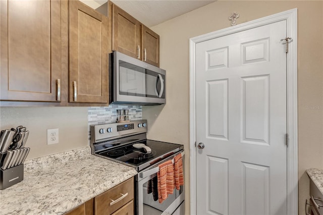 kitchen with appliances with stainless steel finishes, light stone countertops, and backsplash