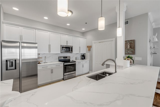 kitchen with appliances with stainless steel finishes, sink, white cabinets, hanging light fixtures, and light stone countertops