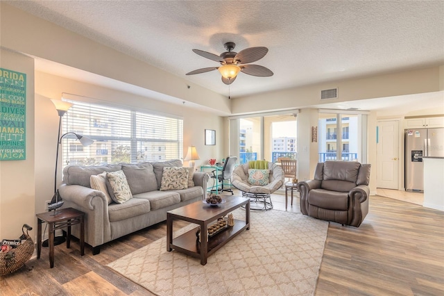 living room featuring ceiling fan, a textured ceiling, and light wood-type flooring