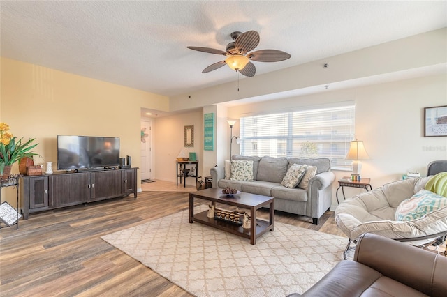 living room featuring ceiling fan, a textured ceiling, and light wood-type flooring