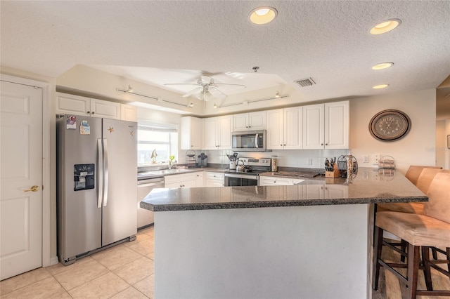 kitchen with appliances with stainless steel finishes, white cabinets, a kitchen breakfast bar, light tile patterned floors, and kitchen peninsula