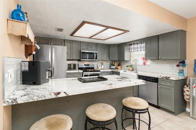 kitchen featuring sink, stainless steel appliances, light tile patterned flooring, decorative backsplash, and kitchen peninsula