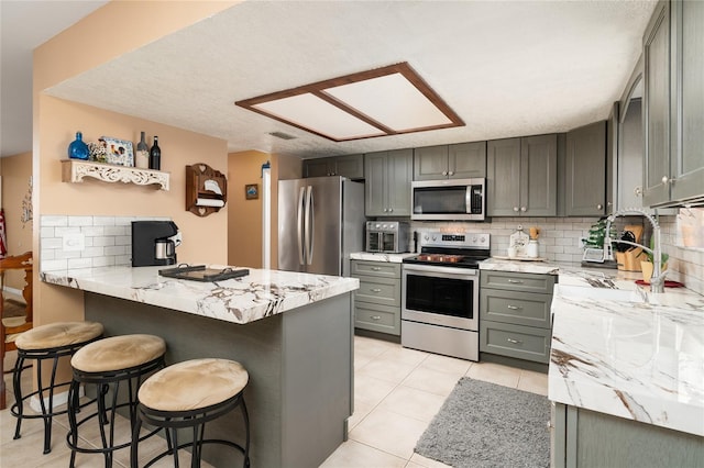 kitchen featuring light tile patterned floors, appliances with stainless steel finishes, a kitchen breakfast bar, kitchen peninsula, and decorative backsplash