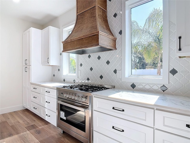 kitchen with white cabinets, high end range, custom exhaust hood, light stone counters, and light wood-type flooring