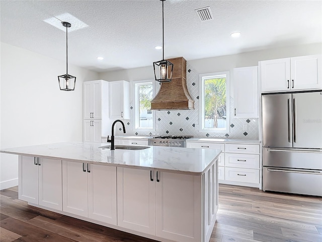 kitchen with a kitchen island with sink, sink, stainless steel fridge, and white cabinets