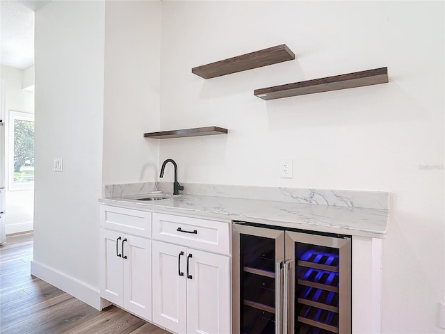 bar with sink, white cabinets, beverage cooler, light stone counters, and light hardwood / wood-style floors