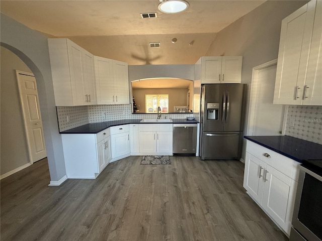 kitchen featuring stainless steel appliances, lofted ceiling, white cabinets, and decorative backsplash