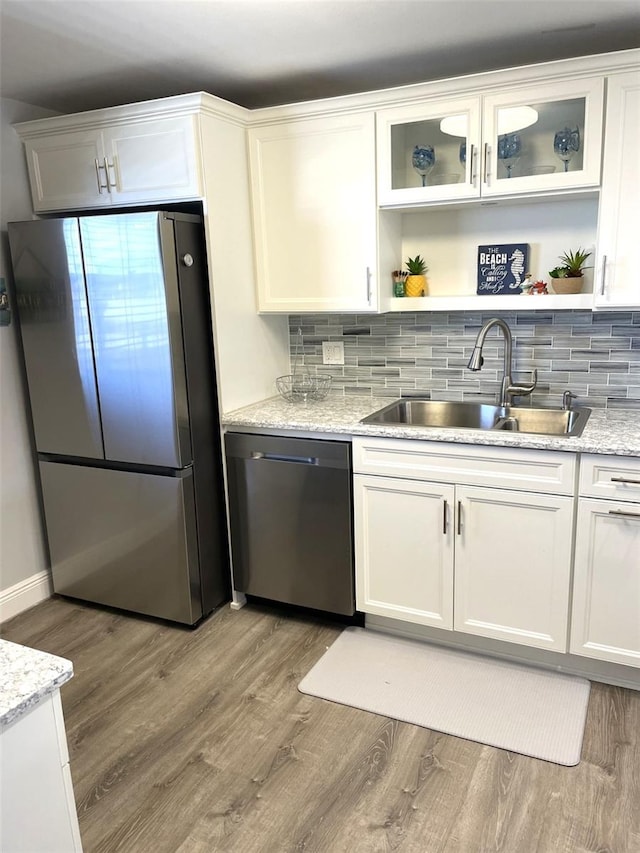 kitchen featuring sink, hardwood / wood-style flooring, appliances with stainless steel finishes, white cabinetry, and light stone countertops