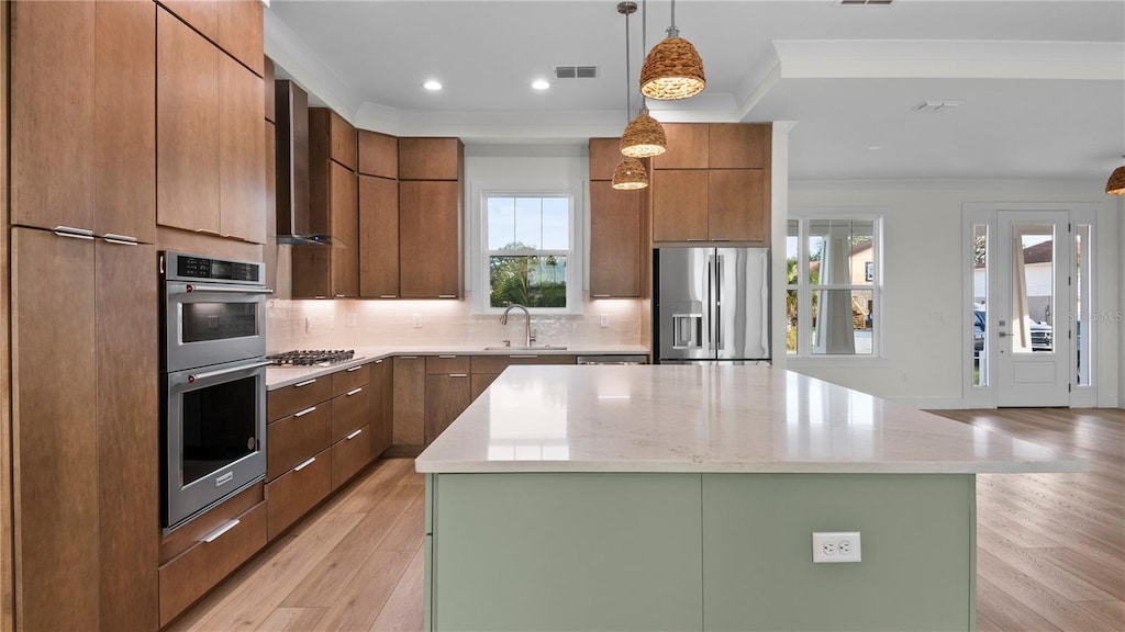 kitchen with a kitchen island, pendant lighting, sink, ornamental molding, and stainless steel appliances