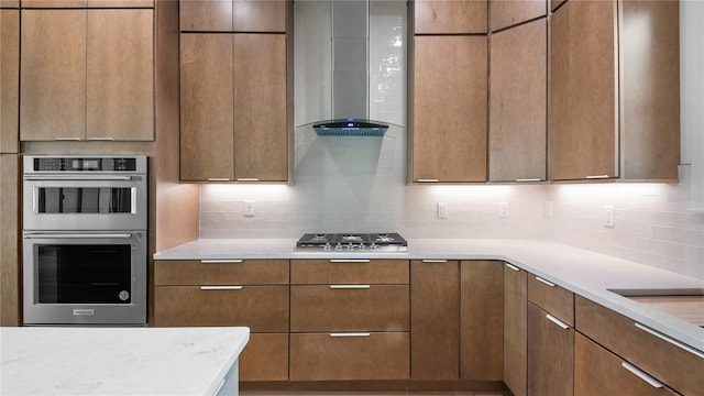 kitchen with appliances with stainless steel finishes, decorative backsplash, light stone counters, and wall chimney exhaust hood