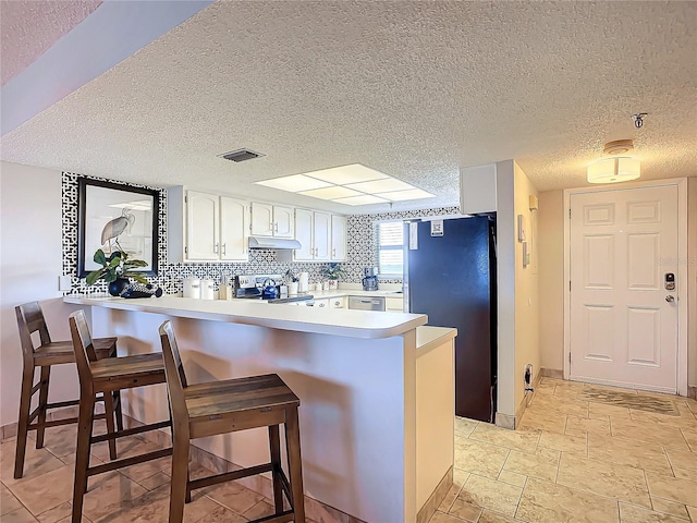 kitchen with a breakfast bar, kitchen peninsula, white cabinets, and refrigerator