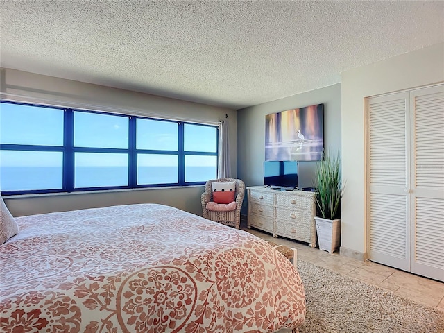 bedroom featuring a water view, a closet, a textured ceiling, and light tile patterned floors