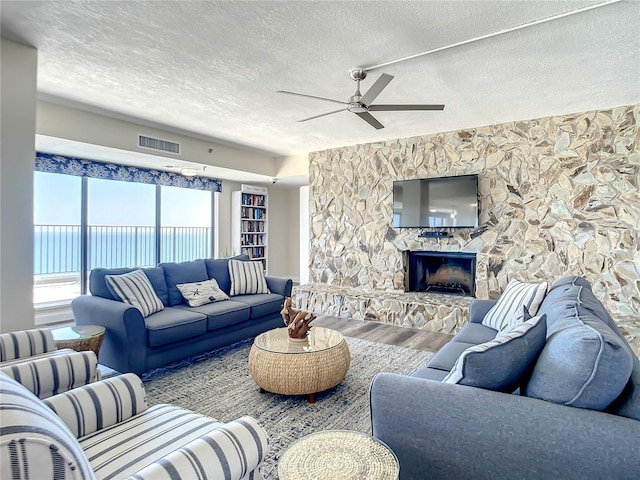 living room with ceiling fan, wood-type flooring, a stone fireplace, and a textured ceiling