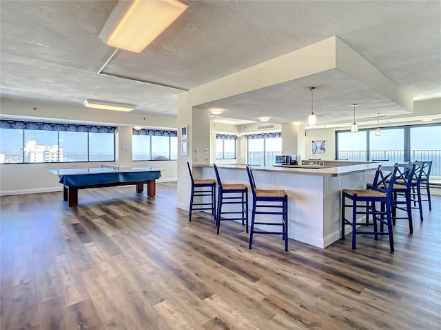 kitchen featuring billiards, a kitchen bar, hanging light fixtures, dark wood-type flooring, and a textured ceiling