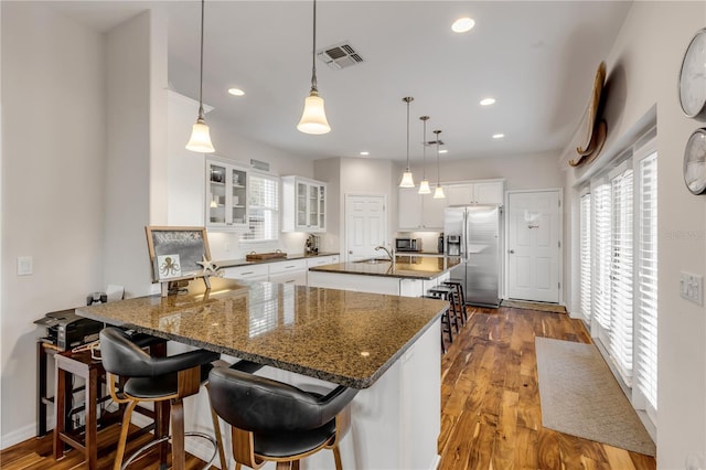 kitchen with white cabinets, a kitchen breakfast bar, hanging light fixtures, a kitchen island with sink, and stainless steel appliances