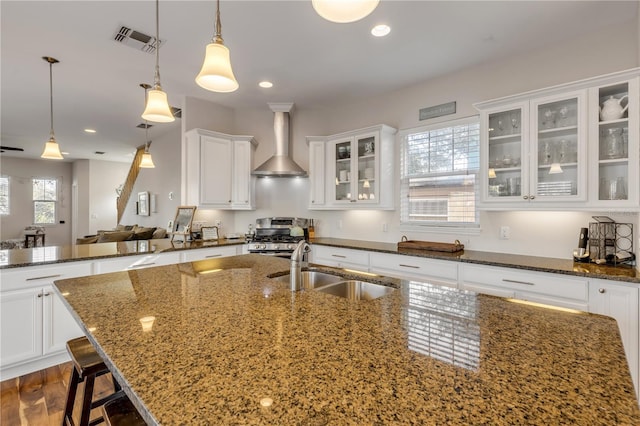 kitchen featuring sink, dark stone countertops, gas range, decorative light fixtures, and wall chimney exhaust hood