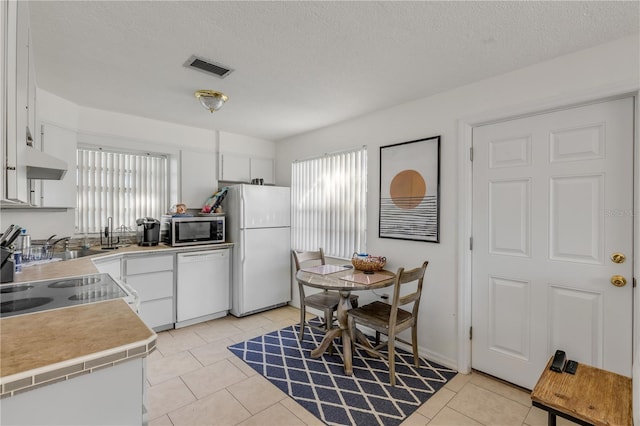 kitchen featuring white appliances, light tile patterned floors, a textured ceiling, and white cabinets