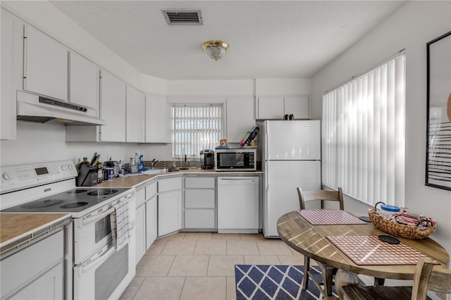 kitchen with white cabinetry, a textured ceiling, light tile patterned floors, tile counters, and white appliances