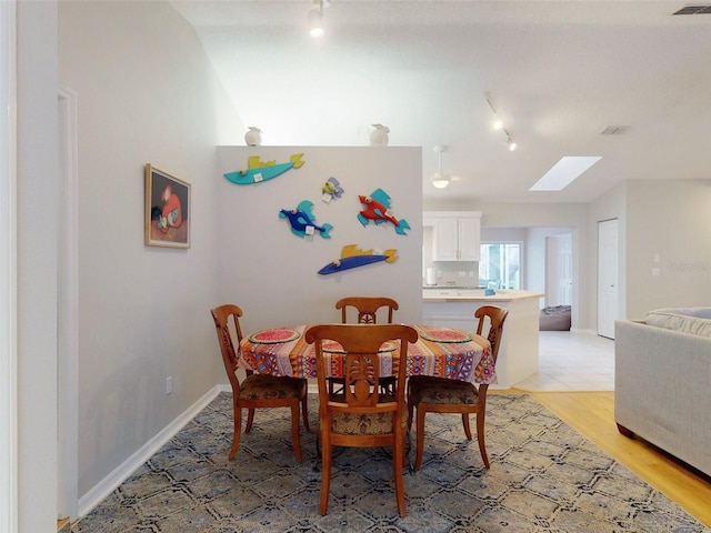 dining space with rail lighting, a skylight, and light hardwood / wood-style floors