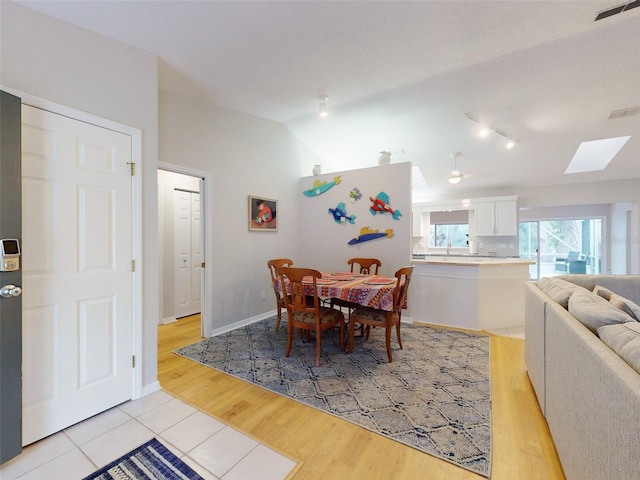 dining area with lofted ceiling with skylight, sink, and light hardwood / wood-style flooring