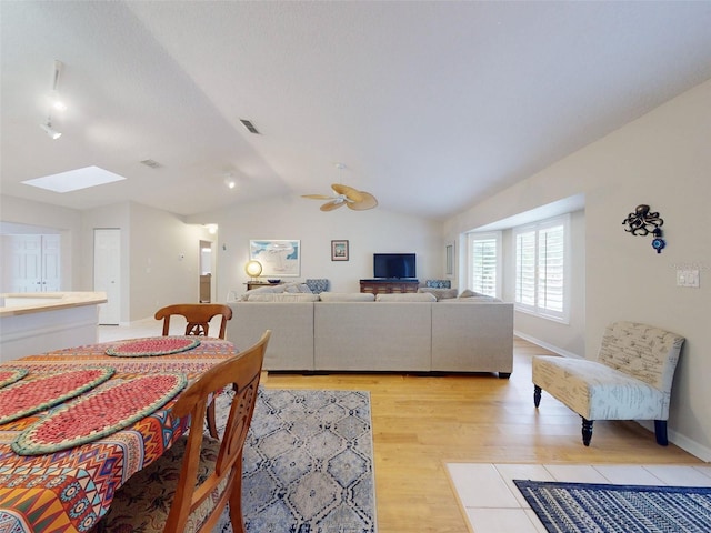 living room featuring lofted ceiling with skylight, ceiling fan, and light wood-type flooring